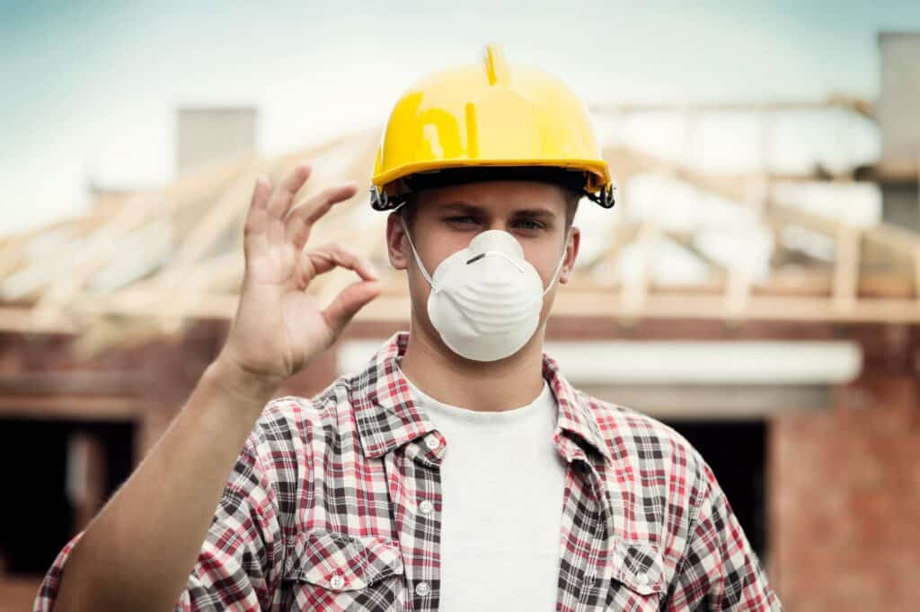 Construction worker wearing a yellow helmet and face mask on site.