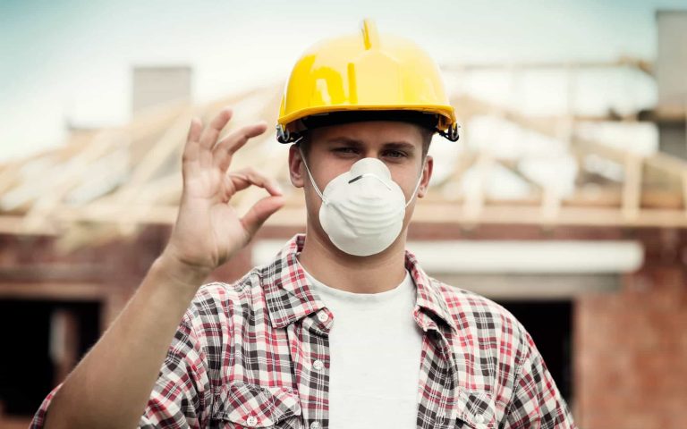 Construction worker wearing a yellow helmet and face mask on site.